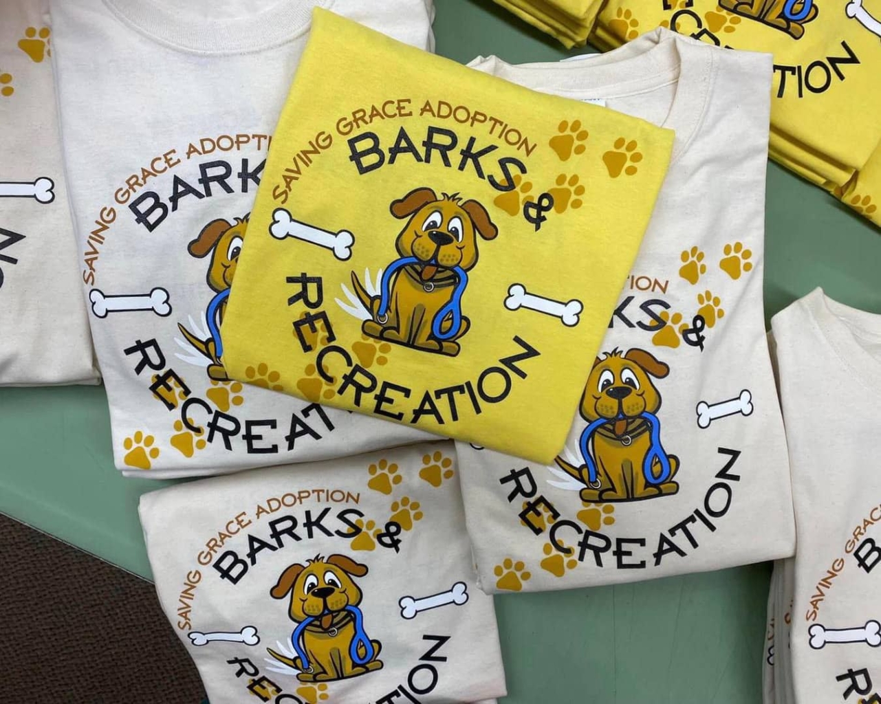 A photo of a stack of Barks and Recreation t-shirts with an illustration of a dog